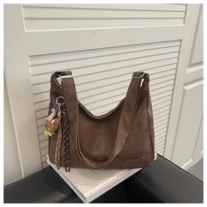 Detail of dark brown matte tote bag with teddy bear charm and braided tassels