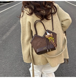 Detail of brown suede tote bag with V-shaped stitching and plush bear charm outdoors