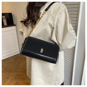 Detail of black glossy leather crossbody bag with gold chain strap on beige trench coat