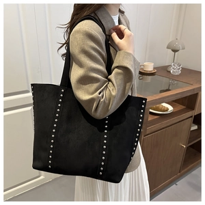 Close-up of black suede tote bag with silver metal rivets and wide shoulder strap