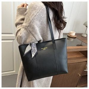 Close-up of black leather tote bag with elegant silk scarf detail and golden logo