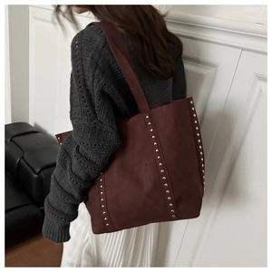 Detail view of burgundy faux suede tote bag with silver rivets carried by a model