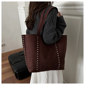 Close-up of a burgundy suede tote bag with silver rivets carried over the shoulder