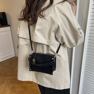 Minimalist black suede crossbody bag with gold hardware shown on a model's shoulder