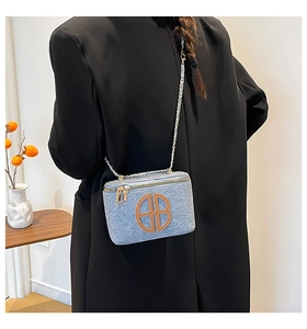 Detail of light blue denim vanity bag with golden chain strap and leather logo detail