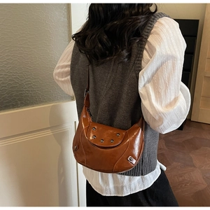 Sac hobo marron avec rivets métalliques porté à l'épaule pour un style vintage