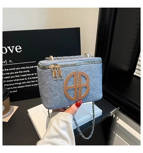 Detail of blue denim square bag featuring AB logo patch and gold chain strap