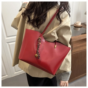 Close-up of red leather tote bag with gold bell charm and woven knot detail on shoulder