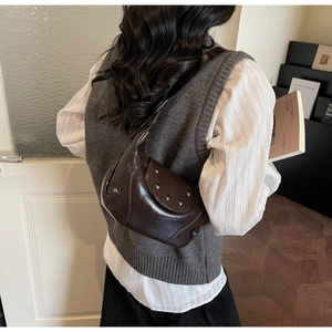 Détail d'un sac à bandoulière vintage marron avec clous métalliques porté par un modèle