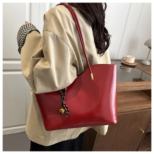 Detail of red glossy leather tote bag with shoulder strap and bell-shaped charm accessory