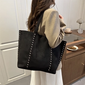 Matte black leather tote bag with silver studs and wide strap in a cozy cafe setting