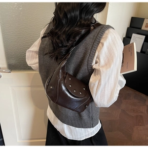 Détail d'un sac à bandoulière marron foncé avec rivets argentés porté par un modèle