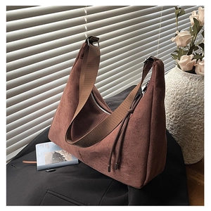 Detail of dark brown suede crescent bag with fringe on a black blazer and flower backdrop