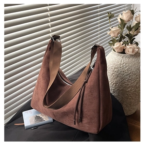 Detail of a brown suede hobo bag featuring a wide fabric strap and vintage side knot