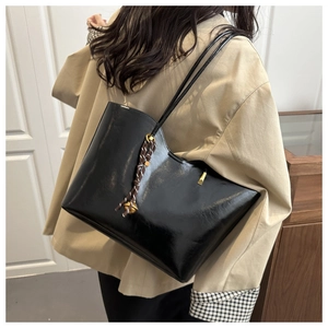 Detail of a large black patent leather tote bag with stylish braided handle accessories