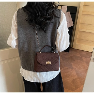 Détail d'un sac bandoulière marron foncé matelassé avec fermoir doré et chaîne