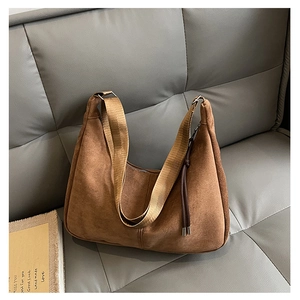 Detail of brown suede crossbody bag with wide nylon strap and tassel on gray sofa