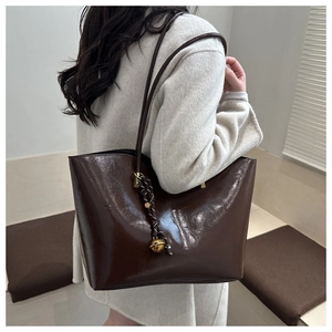 Detail of dark brown glossy leather tote bag with a golden bell charm and woven rope strap