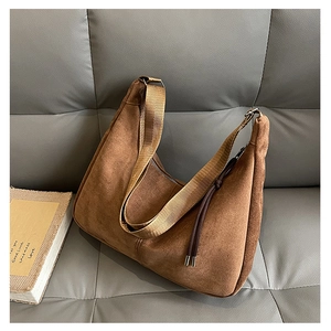 Detail of brown suede crescent bag with wide textile strap on a leather sofa texture