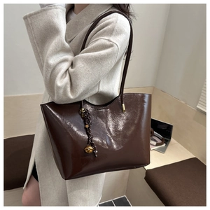 Detail of a dark brown glossy oil-wax tote bag with decorative knot and bell pendant