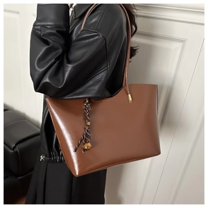 Detail shot of a brown leather tote bag with a decorative bell and rope charm