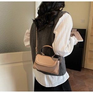 Detail of a beige flap crossbody bag with wide handle and gold hardware on model
