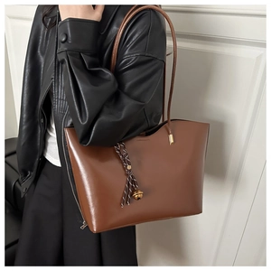 Detail of dark brown tote bag with woven tassel charm shown on a female model