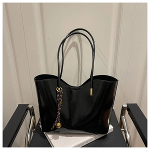 Detail of glossy black tote bag featuring a braided bell pendant on a minimalist chair