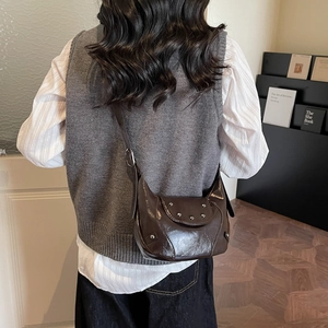 Sac bandoulière marron en cuir brillant avec clous argentés porté par un mannequin