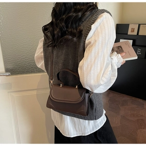 Detail of a dark brown vintage matte leather crossbody bag with curved flap on a model