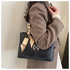 Detail of black leather tote bag with gold M-logo buckle and decorative silk scarf wrap