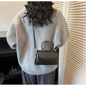 Rear view of model wearing minimalist black faux leather crossbody bag in a home setting