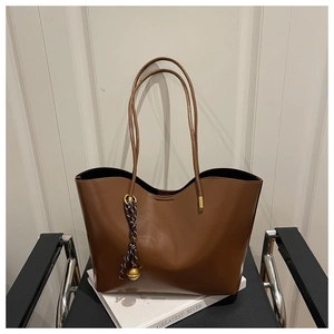 Detail of a brown leather tote bag with gold metal hardware and a decorative pendant