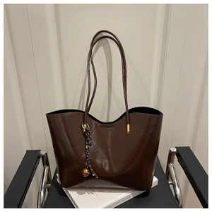 Detail of a dark brown glossy tote bag with dual straps and a decorative bell charm