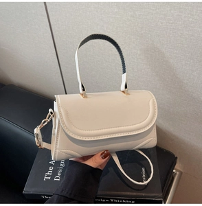 White PU leather small square bag with golden hardware displayed on a book surface