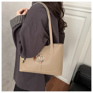 Detail of khaki tote bag with gold M logo and decorative floral scarf on the handle