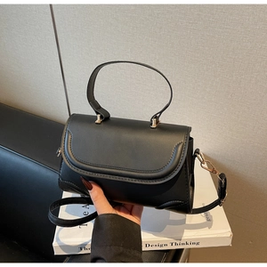 Detailed shot of a black minimalist handbag featuring gold hardware and a leather texture