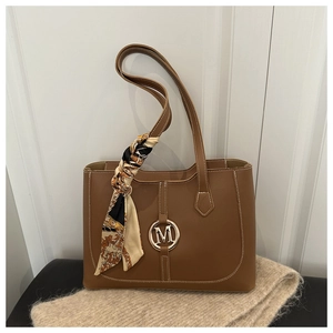 Detail of a brown leather tote bag with M logo hardware and decorative silk scarf accent