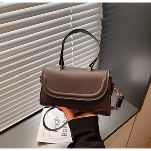 Detail of dark brown leather handbag with curved flap stitching and gold metal hardware