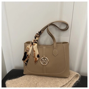 Detail of khaki tote bag featuring gold M logo and decorative printed silk scarf handle