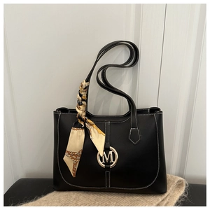 Detail of black leather tote bag with white contrast stitching and golden M logo charm
