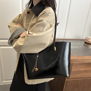 Glossy black leather tote bag with gold bell charm shown in a minimalist interior