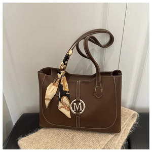 Detail of brown leather tote with golden M buckle and contrast stitching accents