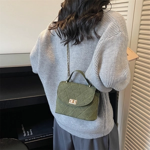Sac à bandoulière matelassé vert foncé avec boucle dorée sur un pull en maille grise