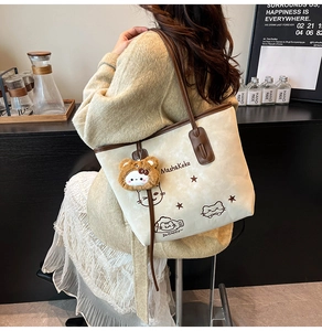 Detail of cream tote bag featuring cartoon cat prints and a brown plush animal charm