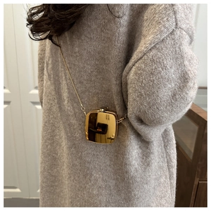 Close-up of a mini gold metallic crossbody bag with chain on a grey sweater