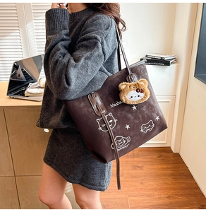 Detailed view of brown suede tote bag featuring cat illustration and plush pendant
