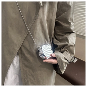 Detail of silver mirror heart mini bag with metallic chain on khaki trench coat