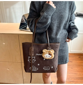 Detail of vintage brown tote bag with cute cat graphic and plush charm on grey sweater