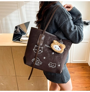 Detail of dark brown tote bag with cartoon cat print and plush bear charm on shoulder